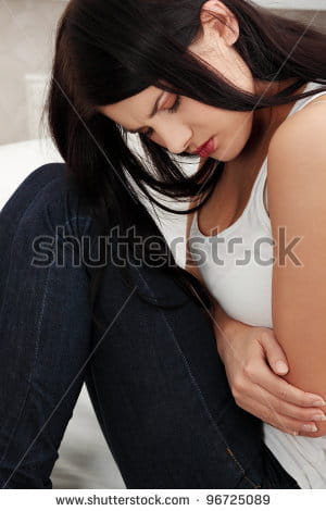 stock-photo-woman-having-a-stomachache-sitting-on-sofa-at-her-home-96725089